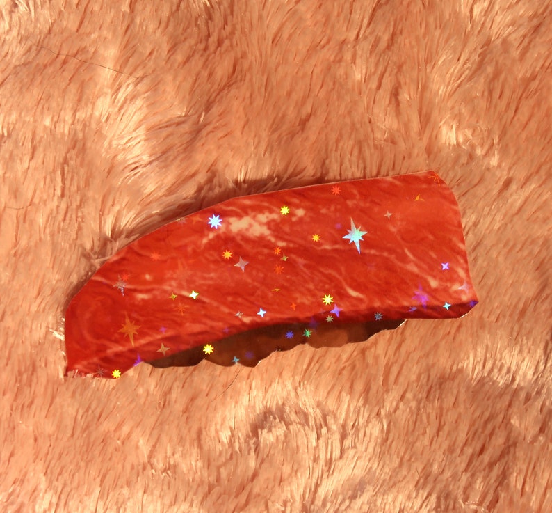 Peut inclure: Un autocollant holographique rouge avec un motif d'&eacute;toiles. L'autocollant a une surface l&eacute;g&egrave;rement textur&eacute;e et une finition brillante.