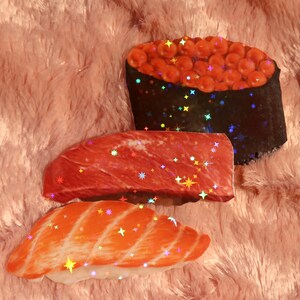 Peut inclure: Trois autocollants de sushi holographiques avec une finition scintillante. Les autocollants repr&eacute;sentent un nigiri au saumon, un nigiri au thon et un maki avec du caviar rouge.