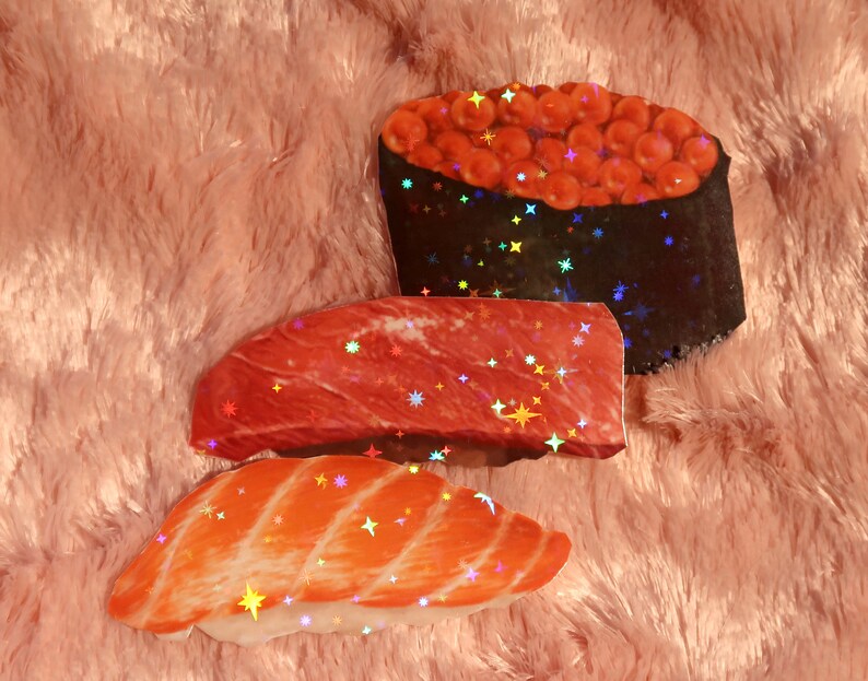 Peut inclure: Trois autocollants de sushi holographiques avec une finition scintillante. Les autocollants repr&eacute;sentent un nigiri au saumon, un nigiri au thon et un maki avec du caviar rouge.