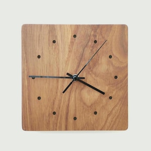 Könnte beinhalten: Quadratische Wanduhr aus Holz mit natürlicher Holzmaserung. Die Uhr hat schwarze Zeiger und schwarze Punktmarkierungen. Das Zifferblatt der Uhr ist warmbraun.