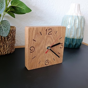Könnte beinhalten: Eine Holzuhr mit schwarzen Zeigern und einem roten Stundenzeiger. Das Zifferblatt der Uhr hat römische Ziffern für 12, 3, 6 und 9. Die Uhr steht auf einer schwarzen Oberfläche.