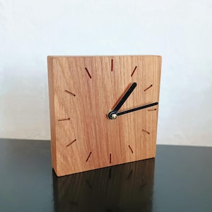 Könnte beinhalten: Eine Holzuhr mit schwarzen Zeigern und einem goldenen Akzent. Das Zifferblatt der Uhr ist aus Holz mit einer Maserung.
