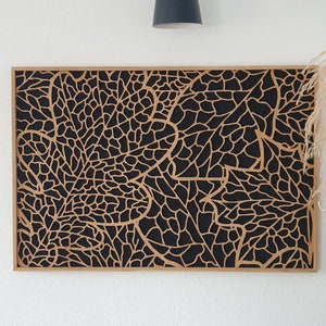Könnte beinhalten: Eine Wanddekoration aus Holz mit einem komplizierten schwarzen und braunen Blattdesign. Das Design ist aus dem Holz geschnitten und erzeugt ein geometrisches Muster.