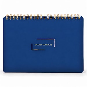 May include: A dark blue weekly schedule planner with a gold wire spiral binding at the top. The front cover features the text "WEEKLY SCHEDULE" printed in gold, centered within a thin gold rectangular frame design.