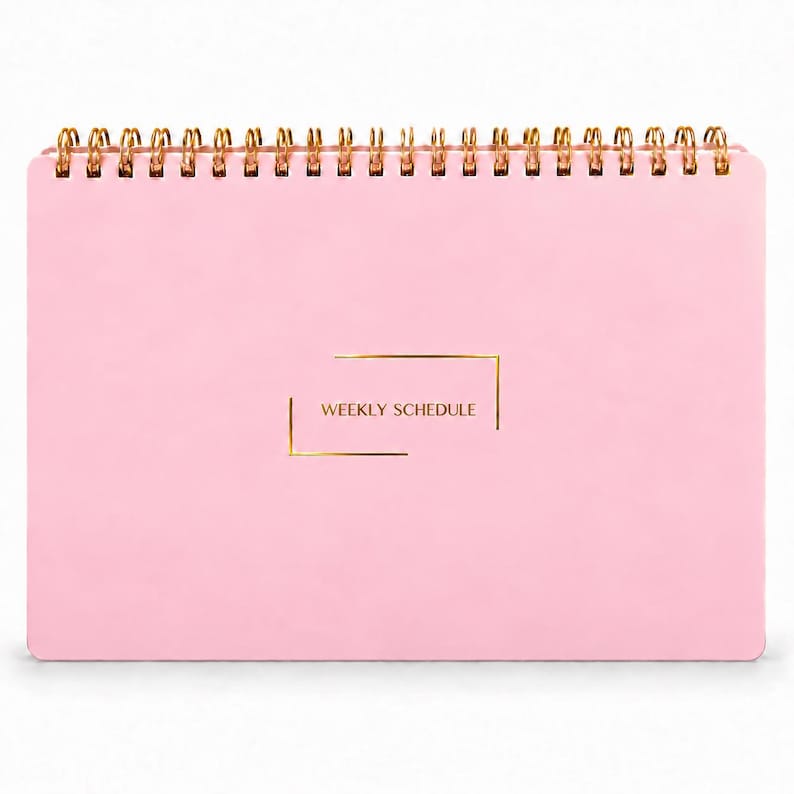 May include: A light pink weekly schedule planner with a gold spiral binding at the top. The front cover features the text WEEKLY SCHEDULE printed in gold, centered within a thin gold rectangular frame with open corners.