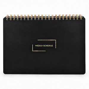 May include: A black weekly schedule planner with a gold wire spiral binding at the top. The front cover features the text WEEKLY SCHEDULE in gold lettering, enclosed within a thin gold rectangular frame design centered on the black surface.