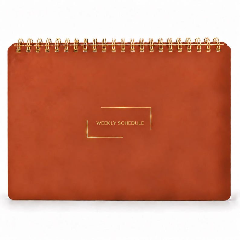 May include: A rust-colored weekly schedule planner with a smooth, matte cover and gold-toned wire-o binding at the top. The center of the front cover features the text WEEKLY SCHEDULE printed in gold, framed by two thin gold rectangular brackets.