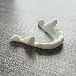 May include: A white 3D printed mouth guard with a textured surface.