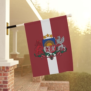 May include: A red, white, and maroon flag with a coat of arms featuring a sun, lions, and a griffin. The flag is hanging from a white pole.