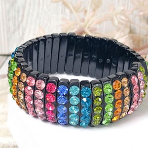 May include: A rainbow-colored stretch bracelet with black elastic and rows of colorful rhinestones.