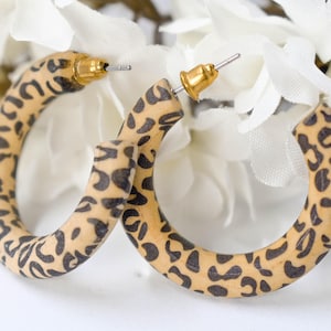 May include: A pair of brown and black leopard print hoop earrings with gold posts.
