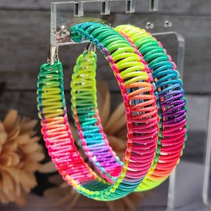 May include: A pair of rainbow colored hoop earrings made of woven thread. The earrings are large and have a bright, colorful design.