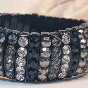 May include: A black elastic bracelet with multiple rows of clear and gray rhinestones.