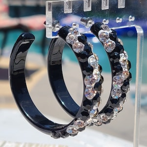 May include: A pair of black hoop earrings with a row of clear rhinestones around the edge.
