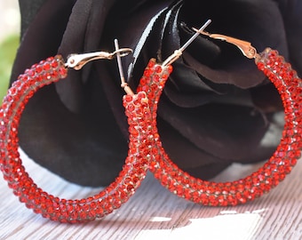 May include: A pair of red hoop earrings with a crystal design. The earrings are made of metal and have a hinged closure.