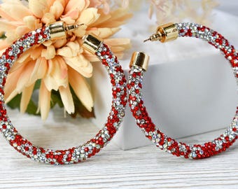 May include: A pair of large hoop earrings with a red and clear crystal design. The earrings are made of metal and have a gold finish.