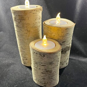 May include: Three birch bark candle holders with LED tea lights. The candle holders are different sizes and are arranged in a pyramid shape.