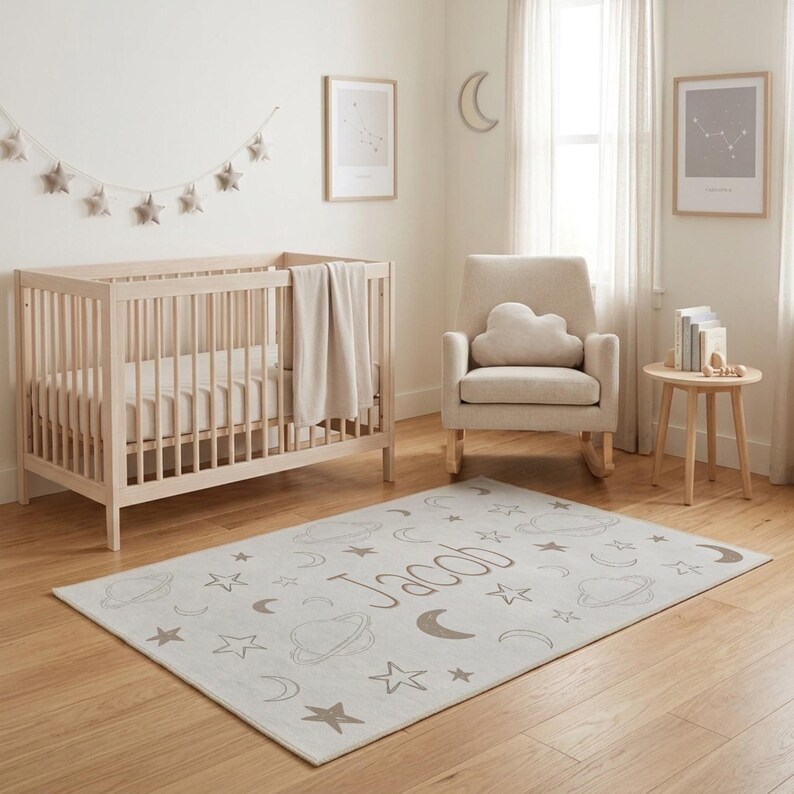 May include: A nursery scene with a light wood crib, a rocking chair with a cloud-shaped pillow, and a rug with a space-themed design. The rug features the name "Jacob" and illustrations of stars, planets, and moons. The room is decorated in neutral tones.