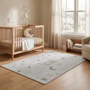 May include: A light gray nursery rug with a celestial design featuring moons, stars, and planets. The name "Noah" is printed in a matching light brown color. A wooden crib and mobile are in the background.