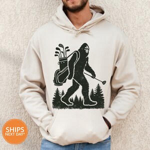 a man wearing a white hoodie with a picture of a bigfoot holding a