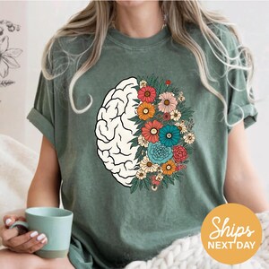 A woman wearing a green t-shirt with a graphic design of a brain surrounded by colorful flowers.