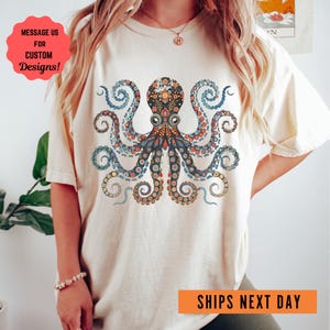 May include: A white t-shirt with a colorful octopus design. The octopus has a floral pattern and is surrounded by swirling tentacles. The text "MESSAGE US FOR CUSTOM DESIGNS!" is in a red circle at the top left of the image. The text "SHIPS NEXT DAY" is in an orange rectangle at the bottom right of the image.