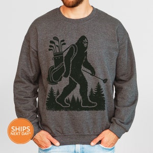 a man wearing a sweatshirt with a picture of a bigfoot holding a golf club
