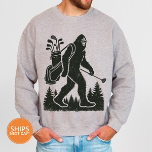 a man wearing a sweatshirt with a bigfoot holding a golf club