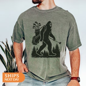 a man wearing a t - shirt with a picture of a bigfoot carrying a