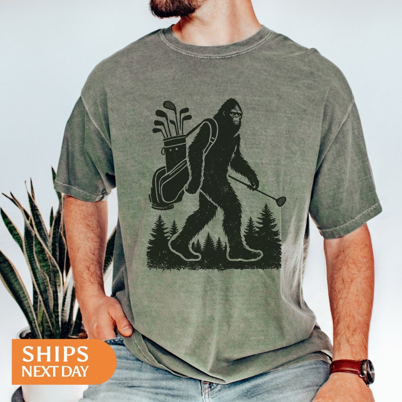 a man wearing a t - shirt with a picture of a bigfoot carrying a