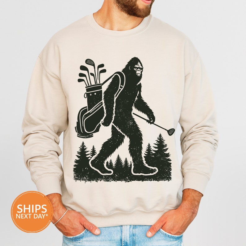 a man wearing a sweatshirt with a bigfoot carrying golf clubs