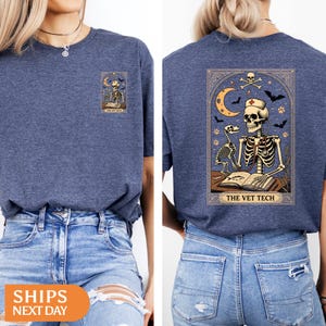 Peut inclure: T-shirt bleu marine avec un motif de carte de tarot. Le motif repr&eacute;sente un technicien v&eacute;t&eacute;rinaire squelette lisant un livre, avec un chien squelette, une lune, des chauves-souris et le texte "THE VET TECH". Le motif est &agrave; l'avant et &agrave; l'arri&egrave;re du t-shirt.