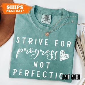 a t - shirt that says, strike for progress not perfection