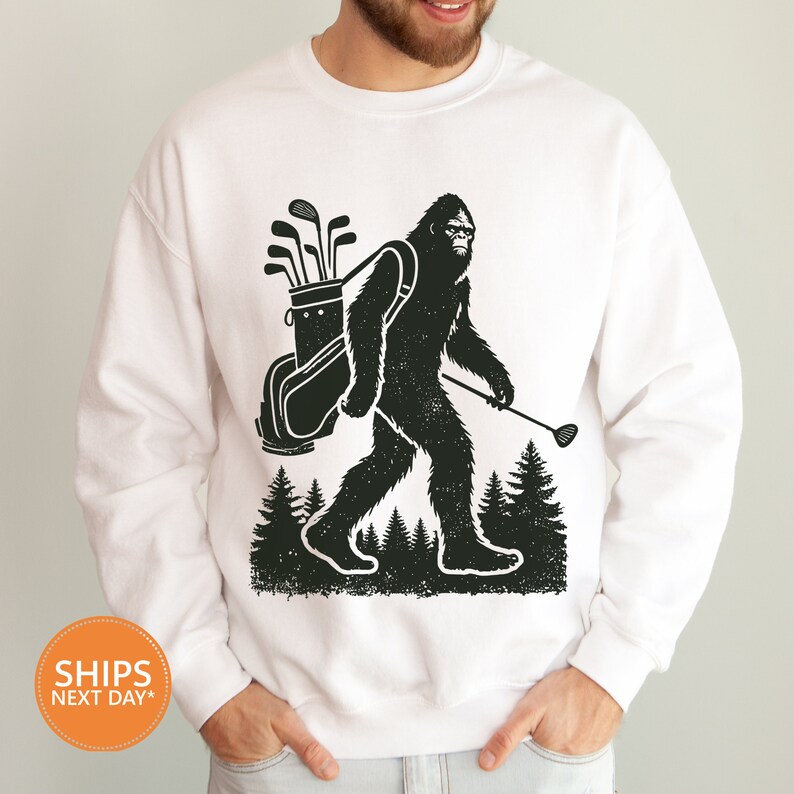 a man wearing a white sweatshirt with a bigfoot holding a golf club