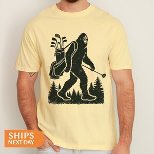 a man wearing a yellow shirt with a bigfoot holding a golf club