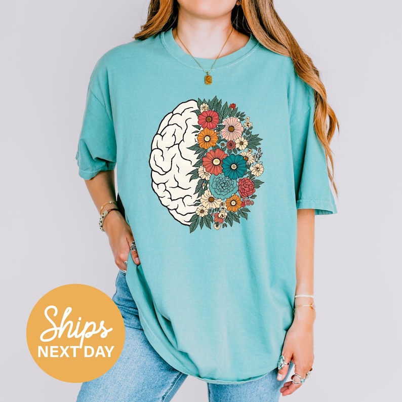 A woman wearing a turquoise t-shirt with a graphic design of a brain surrounded by colorful flowers.
