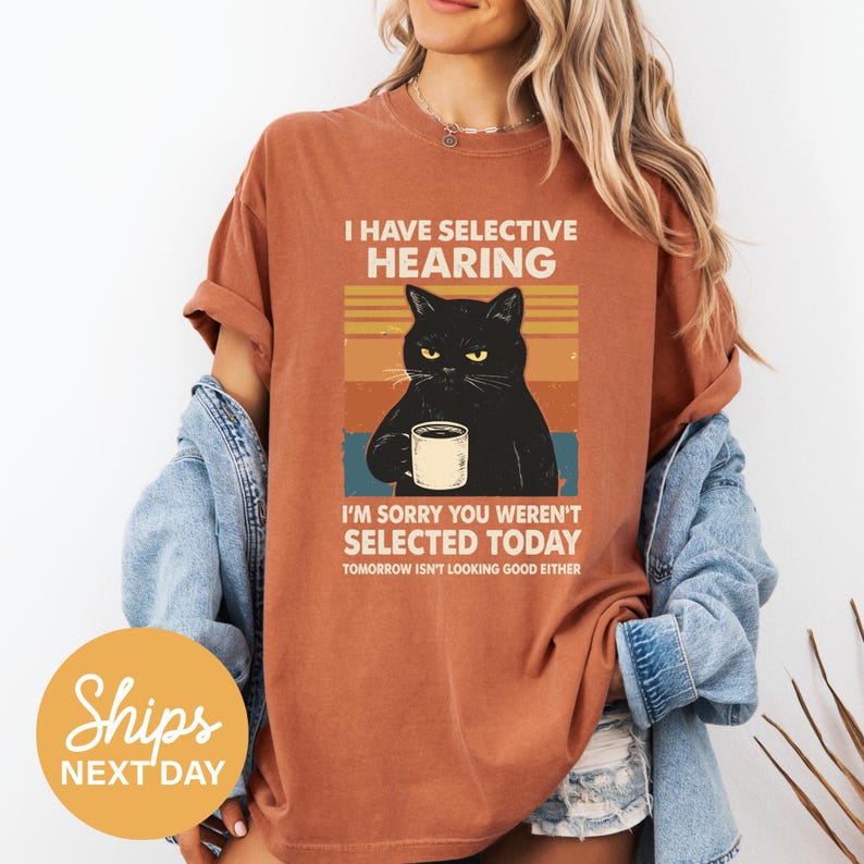 A woman wearing a red t-shirt with a graphic of a black cat and text that reads "I HAVE SELECTIVE HEARING. I'M SORRY YOU WEREnt Selected Today. Tomorrow isn't looking good either."