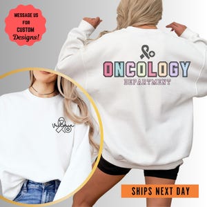 May include: White sweatshirt with the text "ONCOLOGY DEPARTMENT" in rainbow colors and a pink ribbon with a plus sign. The front of the sweatshirt has a small black and white ribbon with a plus sign.