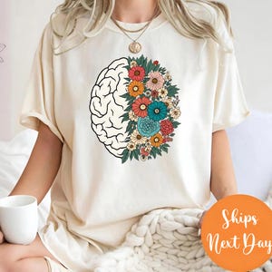 A person wearing a white t-shirt with a graphic design of a brain surrounded by colorful flowers.