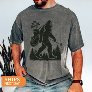 a man wearing a t - shirt with an image of a bigfoot carrying a