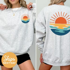 a woman wearing a sweatshirt with a sunset on it