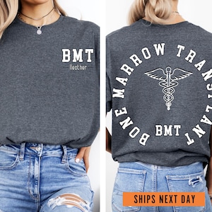 May include: A heather grey t-shirt with the text "BMT - Heather" on the front and "BONE MARROW TRANSPLANT - BMT" in a circle on the back. The back design also includes a caduceus symbol.