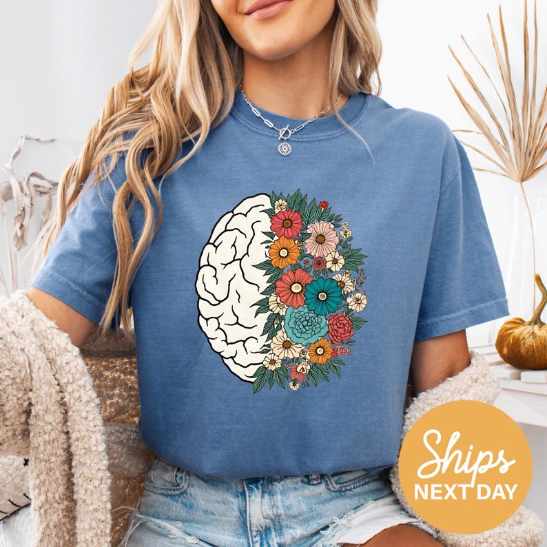 A woman wearing a blue t-shirt with a colorful graphic of a brain surrounded by flowers.