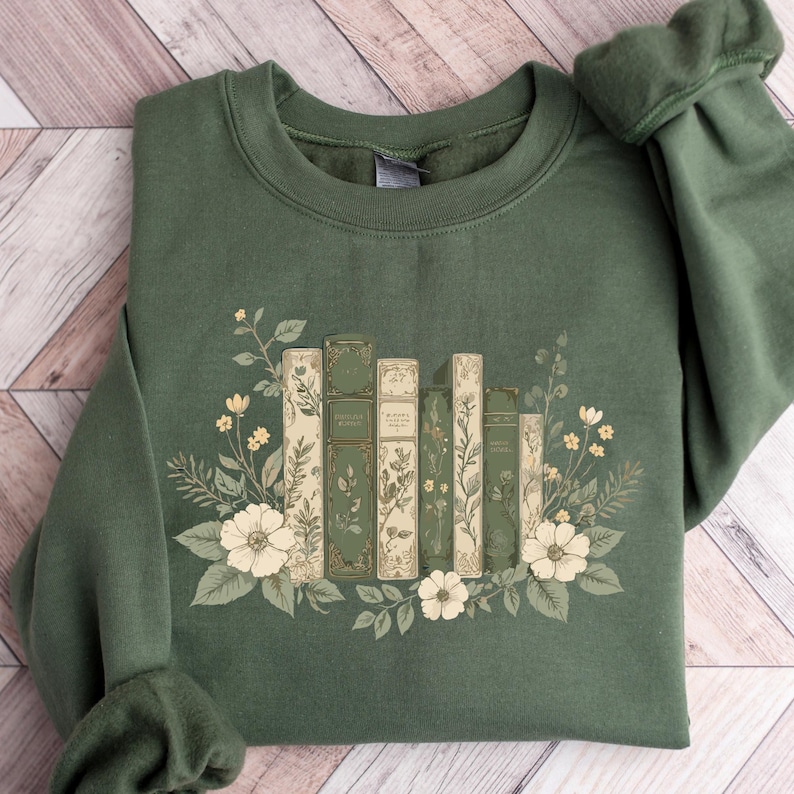 A green sweatshirt with a floral design featuring a row of books surrounded by flowers and leaves.