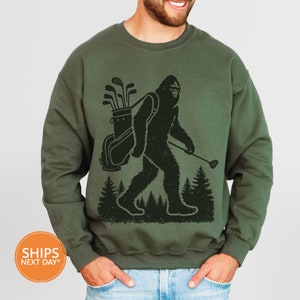 a man wearing a sweatshirt with a picture of a bigfoot holding a golf club