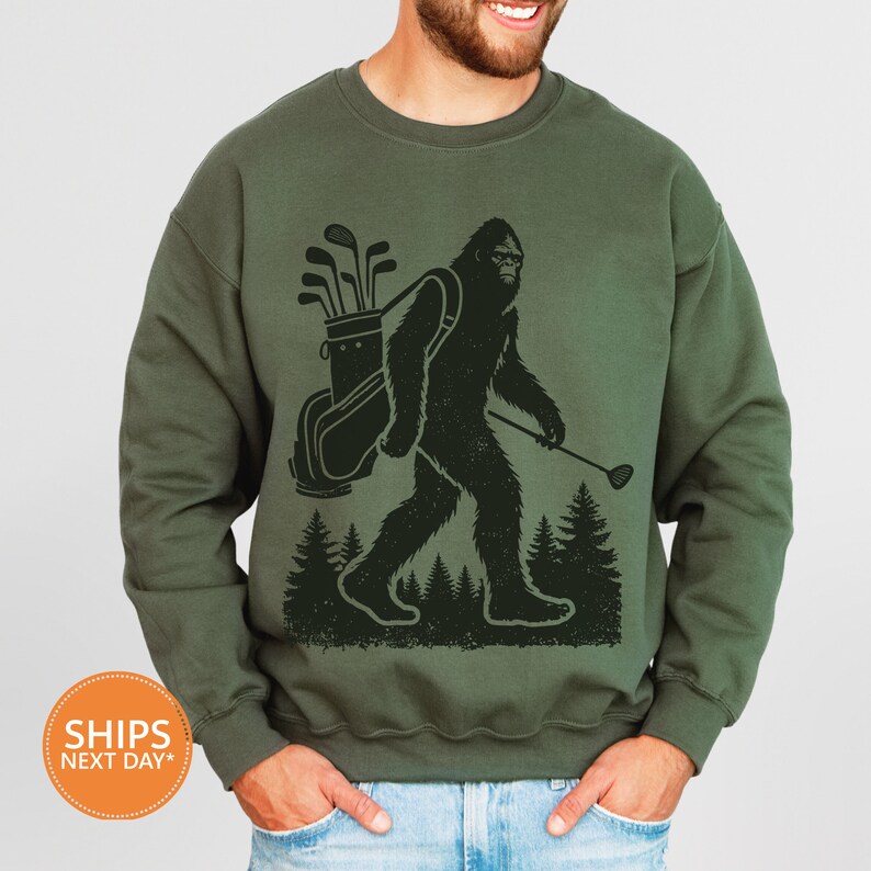 a man wearing a sweatshirt with a picture of a bigfoot holding a golf club