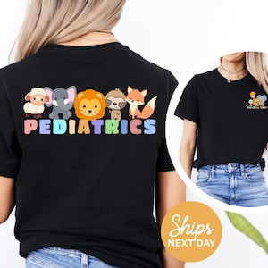 a woman wearing a black t-shirt with a colorful graphic of cartoon animal characters and the word "PEDIATRICS" printed on it.