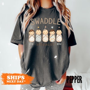 a woman wearing a swaddle t - shirt while standing in front of a
