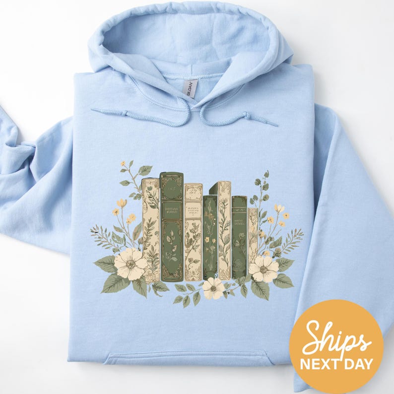 A light blue hoodie with a floral design featuring a row of books surrounded by flowers and leaves.