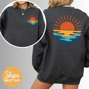 a woman wearing a sweatshirt with a sunset on it